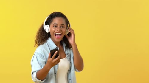 Woman Dancing with Headphones and Phone on Yellow Background