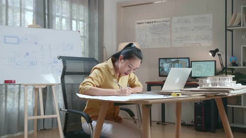 Asian Woman Engineer With A Laptop Drawing Blueprint At The Office