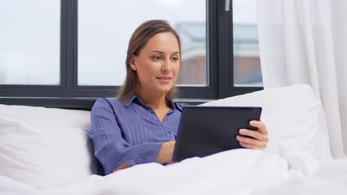 Woman Relaxing in Bed While Using Tablet