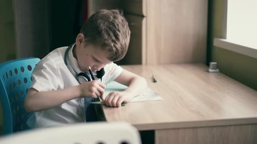 Boy Studies and Writes at Desk Indoors