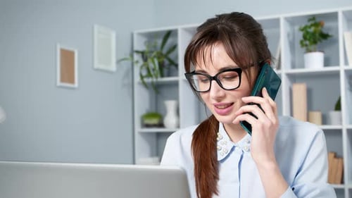 Woman Talking on Phone While Using Laptop at Desk