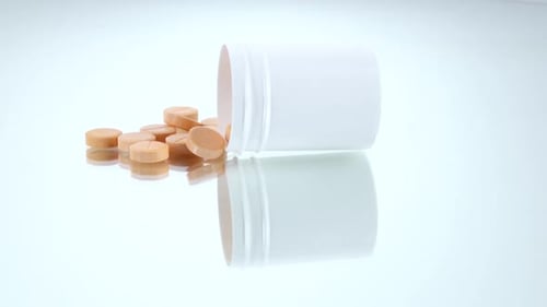 Beige Pills Spilled From a White Pill Container