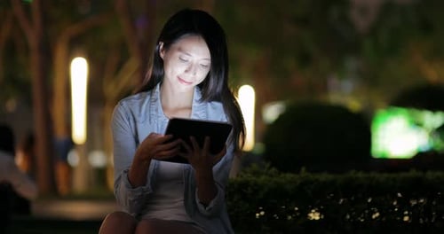 Woman Using Tablet at Night in City Park