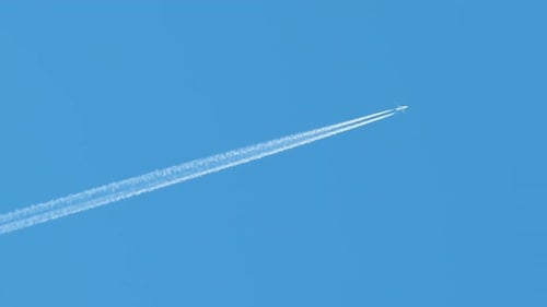Distant Passenger Jet Plane Flying on High Altitude on Clear Blue Sky Leaving White Smoke Trace of