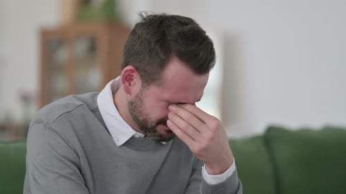 Mann mittleren Alters weint, während er auf dem Sofa sitzt