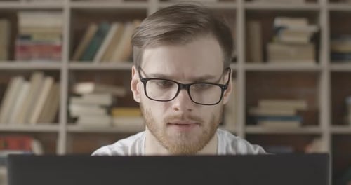 Close-up of Focused Young Man in Eyeglasses Looking at Laptop Screen. Portrait of Caucasian Brunette