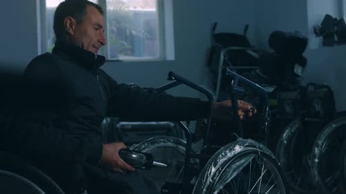 Side View of One American Male Workers in a Workshop at a Factory Making Wheelchairs Sitting at a