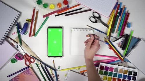 Ein Schüler hält einen Stift und möchte Informationen in ein Notizbuch schreiben, das auf einem Smartphone mit grünem Bildschirm zu sehen