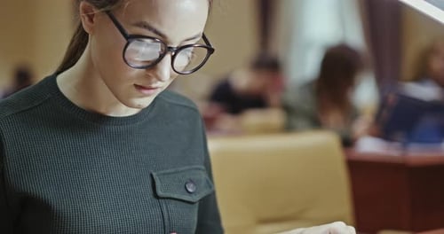 Junge Frau, die in einer Bibliothek arbeitet und ein Buch durchblättert, während sie versucht, Informationen zu finden