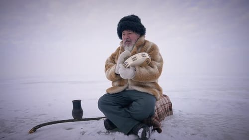 Shaman concentrado tocando tamborim sentado no Oceano Ártico congelado