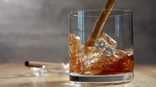 Whiskey being poured into glass with ice and cigar