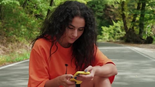 Brunette Woman is Viewing Photos in Smartphone Outdoors in Park