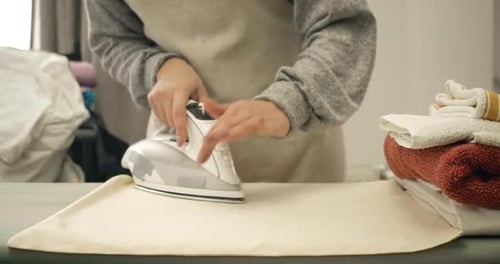 Close-up of Female Caucasian Hands Ironing Laundry Indoors. Unrecognizable Young Woman Doing