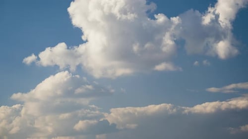 Time lapse footage of fast moving white puffy clouds on blue clear sky.