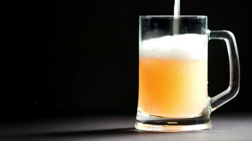 Processo de enchimento de uma enorme caneca de vidro com bebida alcoólica espumosa de malte isolada em fundo preto