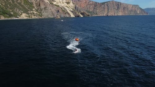 Jet Ski Pulling Raft on Water near Cliffs