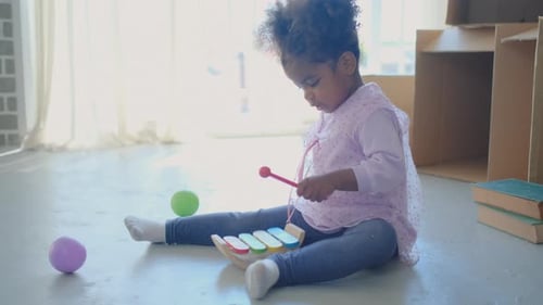 Young Girl Plays Xylophone on Floor