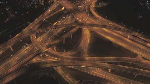 Entroncamento rodoviário complexo iluminado e tráfego de carros à noite. O drone está orbitando ao redor. Vista aérea