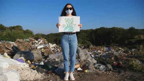 Young Woman Holds Sign at Landfill Site