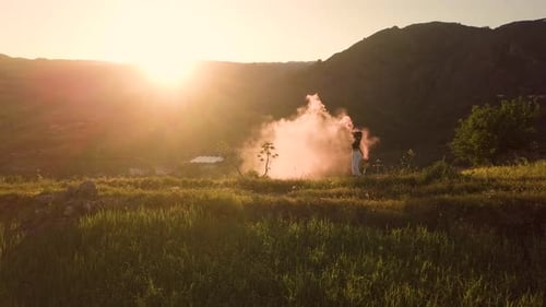 Woman with Flare Walking in Grassy Field at Sunset