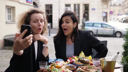 Two Young Women Eating Lunch Using Smartphone
