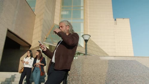 Mature Man Using Phone Near Office Building