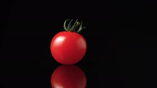 Eine reife rote Tomate mit grünem Schwanz rotiert langsam auf einer schwarzen reflektierenden Küchentischoberfläche