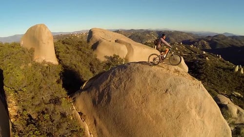 Aerial shot of young man mountain biker resting with his bike on a boulder.