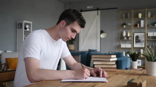 Young Adult Writes on Paper at Table