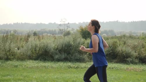 Woman Jogging Outdoors in Green Grassy Park