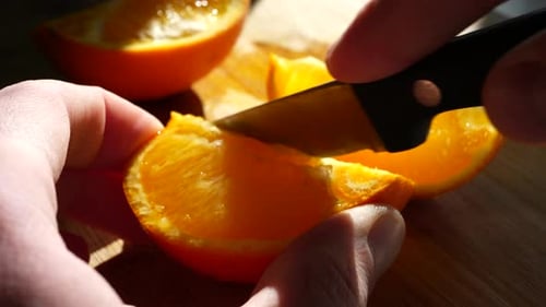 Cutting a ripe orange fruit slice with a knife in the sunlight on a cutting board for a healthy snac