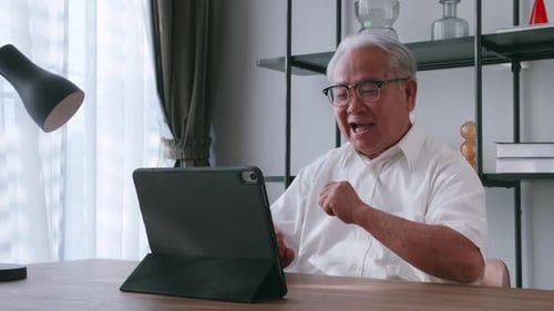 An elderly Asian man having video call with family on tablet computer at home.
