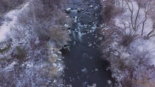 Looking straight down at a river rushing through a winter scene and panning up to reveal more of the