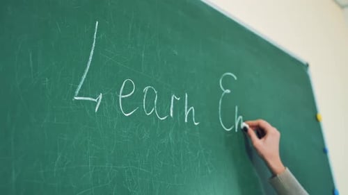 Close-up of a hand with a chalk writing the word English. Woman's hand holding chalk