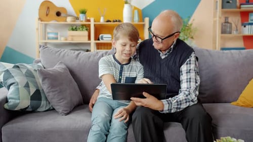 Grandfather and Grandson Enjoying Tablet Indoors on Couch