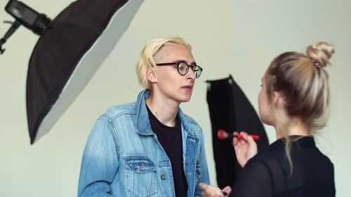 Le maquilleur corrige le teint du petit ami du mannequin en lui parlant. L'acteur blond
