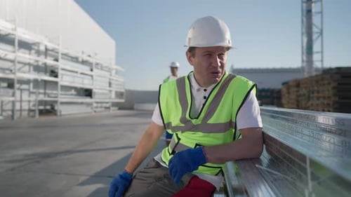 Portrait of Tired Overworked Caucasian Man in Hard Hat Sitting Down Rubbing Forehead