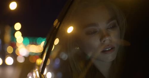 Young Girl Uses a Smartphone, Sitting on Back Seat of a Car, Night Road in the City, Reflection of