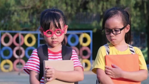 Two cute schoolgirls wearing summer clothes with backpacks walking together in the school