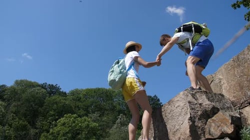 Man Helps Woman Climb Up Rocky Hill