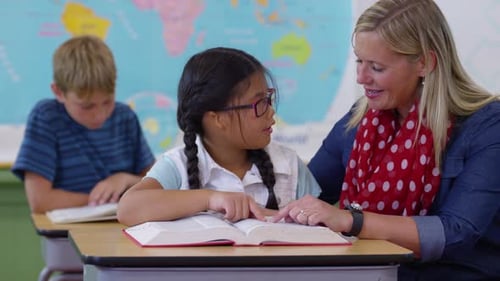 Teacher Helping Student Read in Elementary Classroom