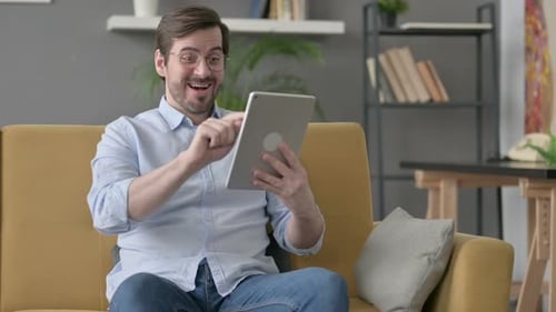 Young Adult Using Tablet Celebrating on Couch