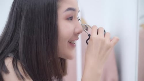 Woman Curls Eyelashes in Mirror With Metal Curler