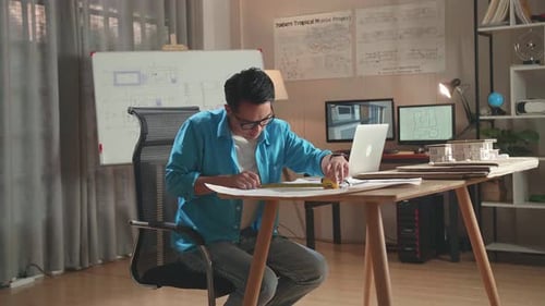 Asian Man Engineer With A Laptop Measuring Blueprint At The Office