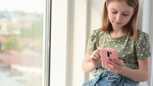 Girl Using Smartphone Sitting by Window