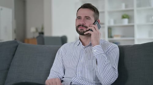 Bearded Man Talking on Smartphone While Sitting on Sofa
