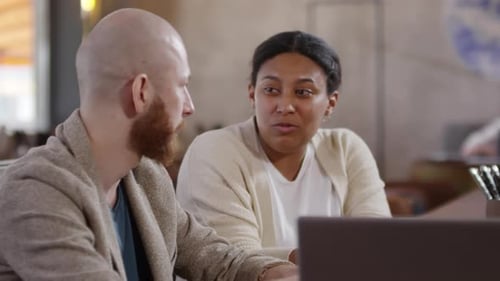 African Woman Discussing Project on Laptop with Male Colleague in Cafe