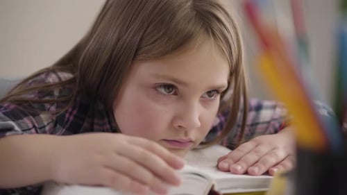 Close-up of Pretty Caucasian Brunette Girl with Brown Eyes Holding Head on Book. Tired Schoolgirl