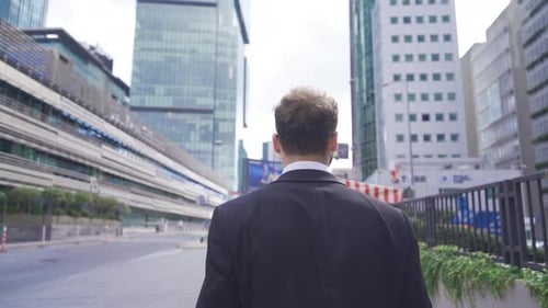 Homme d'affaires attrayant et confiant marchant près d'un immeuble de bureaux moderne.