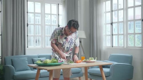 Asian Man Holding A Knife And Slicing Broccoli And Carrot While Cooking Healthy Food At Home